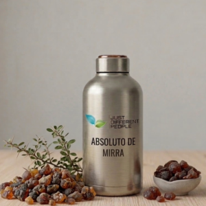 Stainless steel bottle labeled 'Just Different People' with 'Absoluto de Mirra' beside a pile of amber stones and a small bowl, on a wooden surface with a sprig of green leaves.