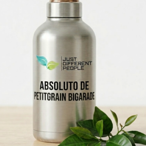 Silver stainless steel bottle with the label 'ABSOLUTO DE PETITGRAIN BIGARADE' and a 'Just Different People' logo with two green leaves, on a wooden surface with greens nearby