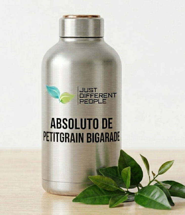 Silver stainless steel bottle with the label 'ABSOLUTO DE PETITGRAIN BIGARADE' and a 'Just Different People' logo with two green leaves, on a wooden surface with greens nearby